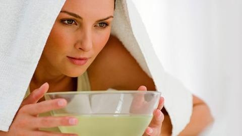 Eine Frau inhaliert mit einem Handtuch über dem Kopf