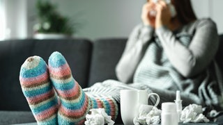 Frau in einem Berg aus Taschentüchern und Erkältungsmitteln