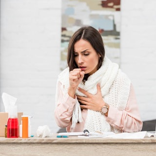 Hustende Frau. Hustenreiz und abgeschlagen: Wie lassen sich Beschwerden durch gereizte Atemwege lindern, wann ist ein Arztbesuch nötig? Welche Hausmittel helfen, und wann Antibiotika nötig sind.