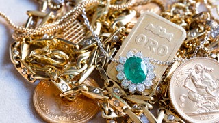 In einer Nahaufnahme liegen goldene Münzen, Ketten und Armreifen auf einem Haufen. Grün unterlegt steht der Titel: Schmucl, Münzen & Co.:Wie Fair geht es beim Goldankauf zu?