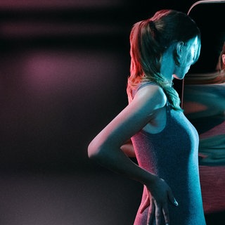 Junge schlanke Frau steht vor Spiegel und nimmt ihren Körper verzerrt wahr