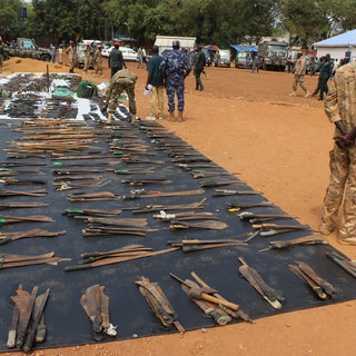 Waffen liegen ausgebreitet auf einer Plane hinter einem sudanesischen Soldaten