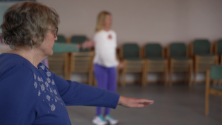 Ältere Dame macht Übungen mit einer Übungsleiterin im Hintergrund