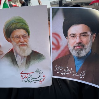Eine Frau hält Plakate von Ayatollah Modschtaba Chamenei (r), dem Nachfolger seines getöteten Vaters, Ayatollah Ali Chamenei (l)