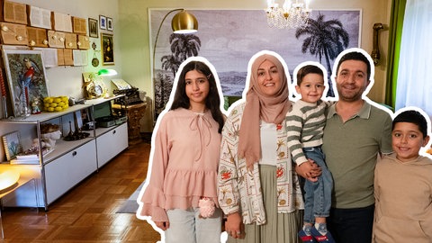 Ayşe steht mit ihrem Mann und ihren drei Kindern in ihrem Wonhzimmer, das sie in einem Stilmix aus großen Prints, alten Lampen und bunten Farben eingerichtet hat.