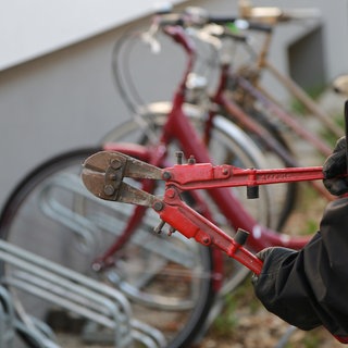 Bolzenschneider in der Hand eines Diebes vor einem Ständer mit Fahrrädern. Gute Fahrradschlösser können vor Fahrraddiebstahl schützen.