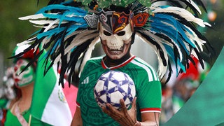 Ein maskierter Mann mit Mexiko Trikot und Fußball während einer Parade in Mexiko Stadt im März 2026