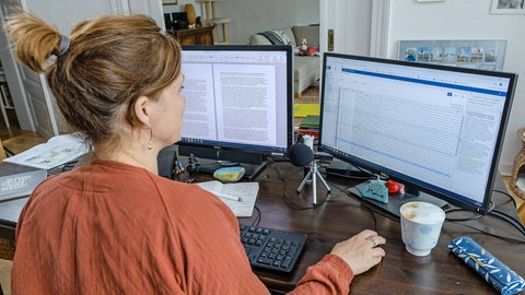 Eine Frau sitzt im Homeoffice vor zwei Bildschirmen in einer Wohnung